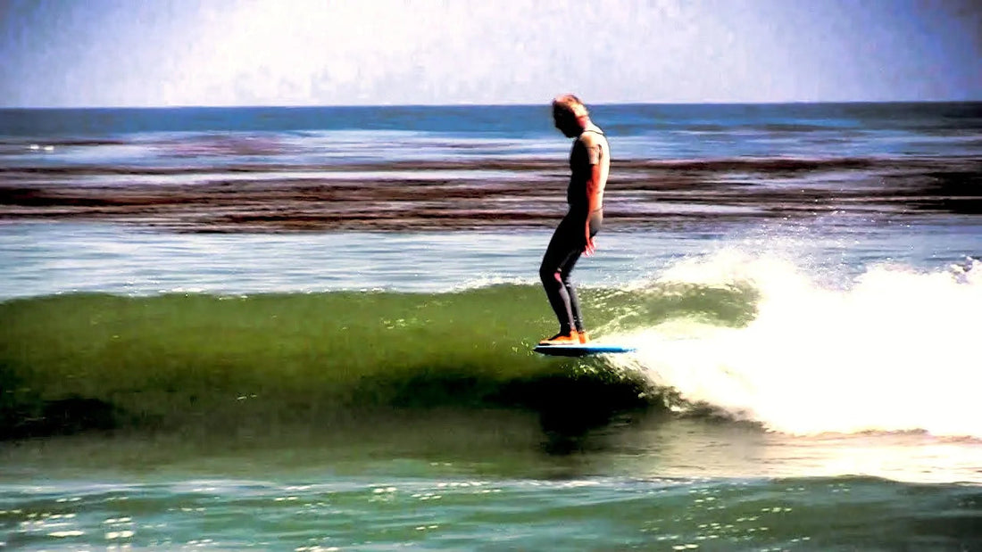 Surfer in black wetsuit riding a wave on a blue surfboard on a sunny ocean day