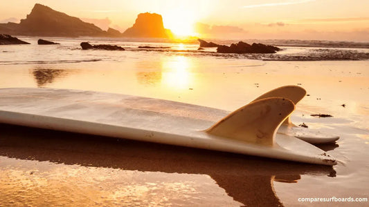 White surfboard with fins on wet sandy beach at sunset with ocean and rocky islands in background