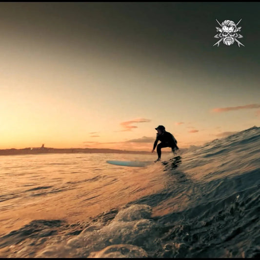 Surfer riding wave at sunset with a coastal city skyline in the background
