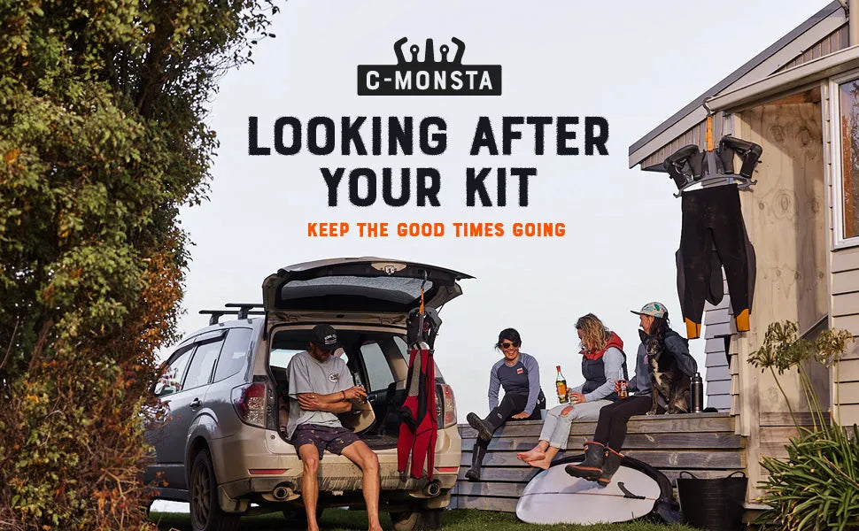 Group of people relaxing near car and small building with wetsuits, surfboard, and dog outdoors
