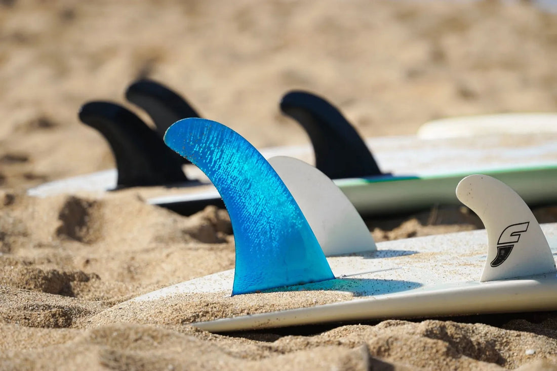 Close-up of surfboard fins in sand on a beach, featuring blue and black fins