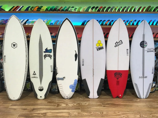 Row of six assorted surfboards with logos and colorful fins displayed on shelves in surf shop