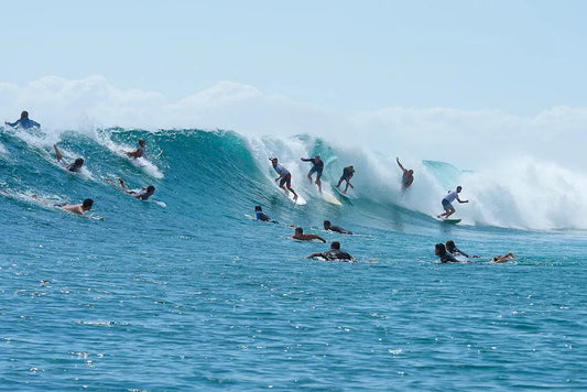 Group of surfers catching large blue ocean waves under clear sky