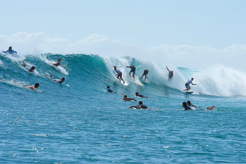 Group of surfers catching large blue ocean waves under clear sky
