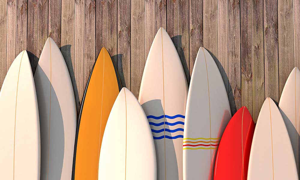 Various colorful surfboards leaning against a wooden fence in bright sunlight