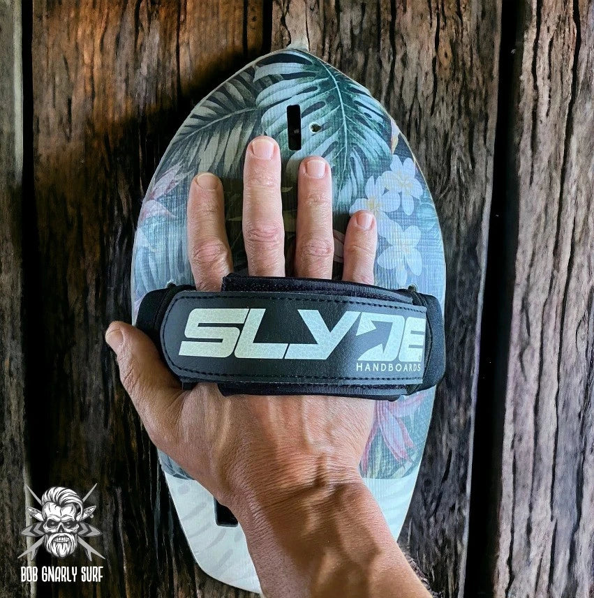 Hand wearing a tropical floral patterned SLY handboard on rustic wooden surface for bodysurfing