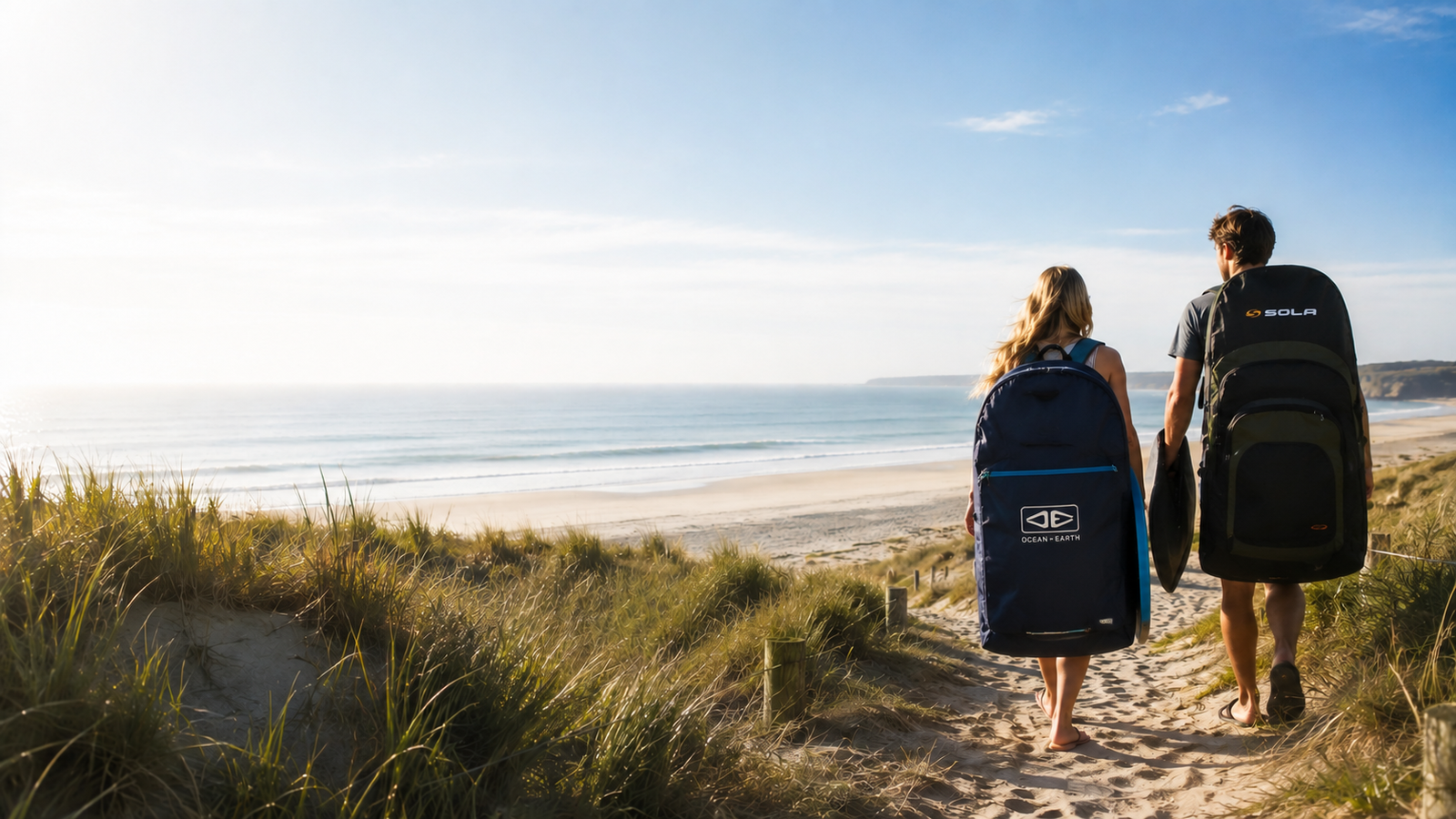 Black and green Sola triple bodyboard bag standing on sandy beach with rocky coastline and blue ocean background