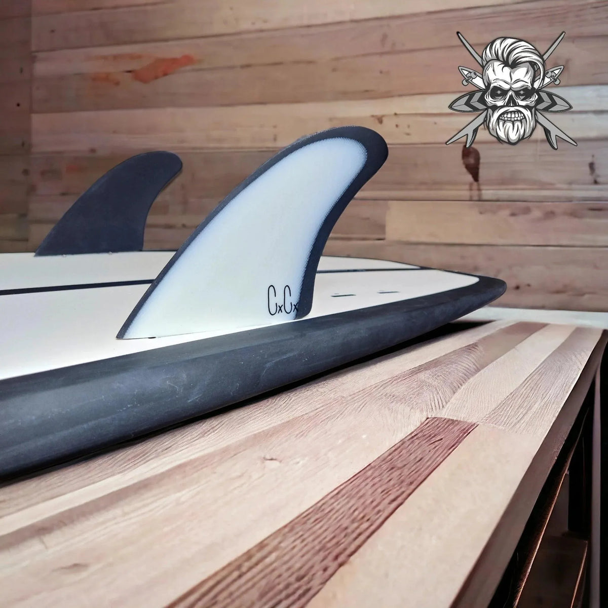 Close-up of black and white twin surfboard fins on a white surfboard with wooden wall background