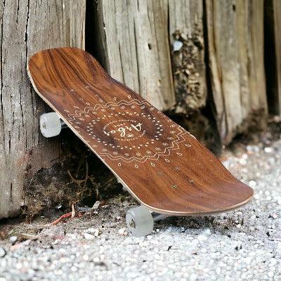 Wood-grain skateboard with intricate circular floral design leaning against weathered wooden posts on gravel surface