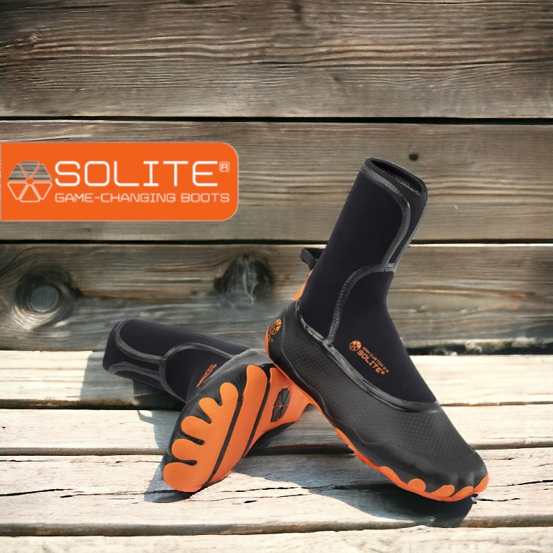 Black and orange Solite neoprene water boots on wooden surface with logo in background