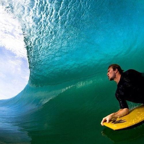 Surfer paddling on yellow board inside a large blue ocean wave barrel under sunlight