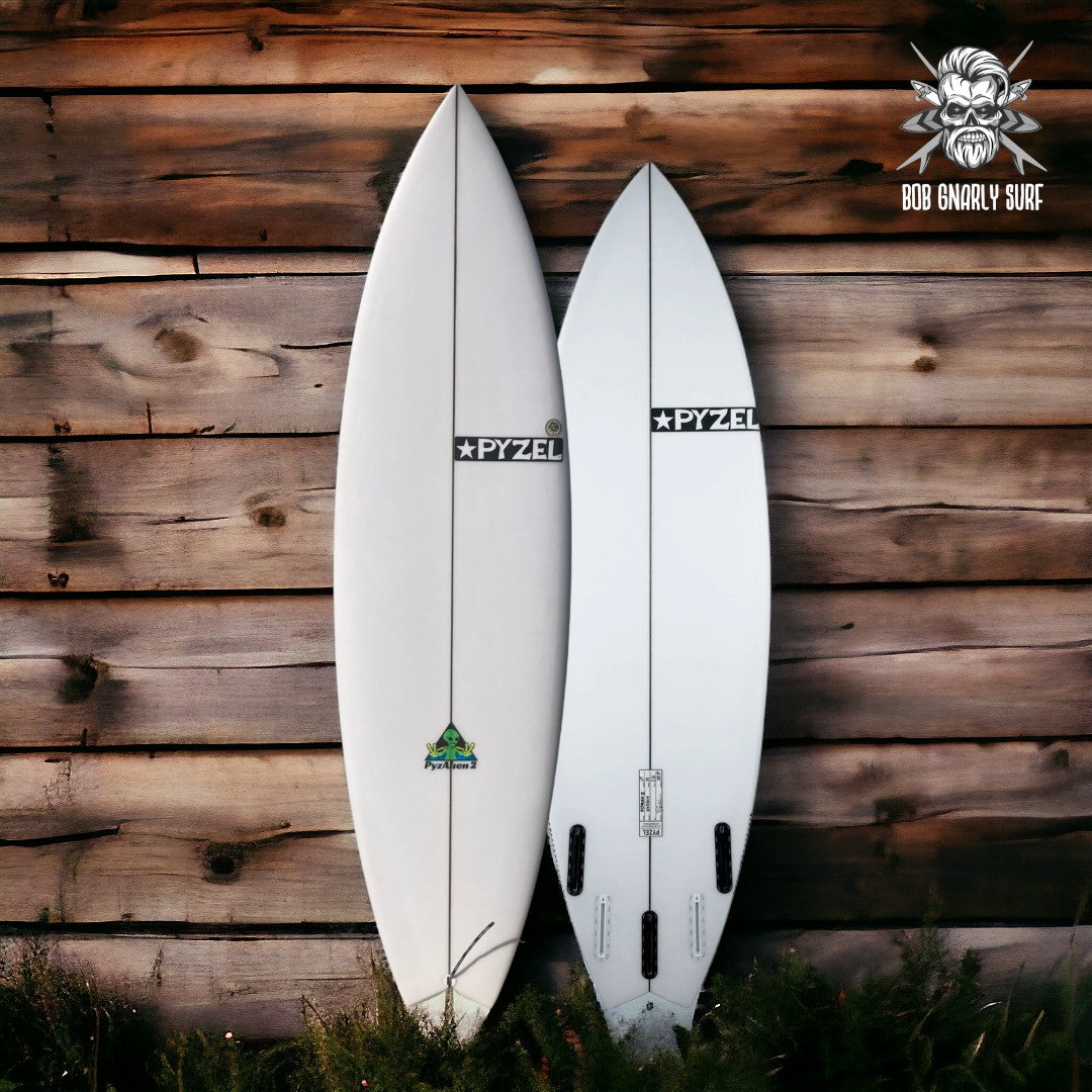 Two white Pyzel surfboards leaning against wooden wall, Bob Gnarly Surf logo in top right corner